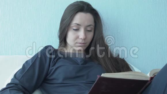 年轻女子坐在床上看书望着窗外美丽的年轻女子躺在床上看书视频的预览图
