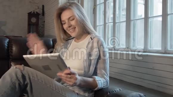一位美丽的年轻女性通过Skype通过平板电脑进行交流他向摄像机挥手笑了一个金发女郎视频的预览图