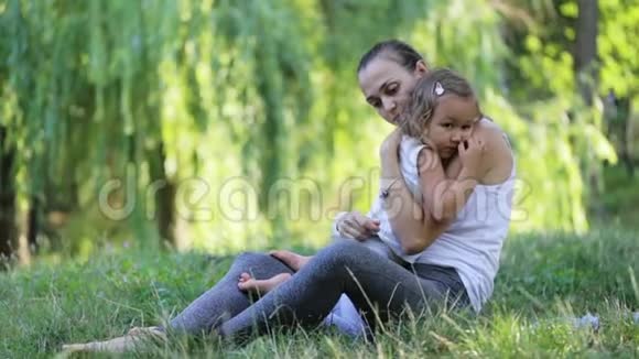 在绿色公园做瑜伽运动时母亲和女儿坐在一起拥抱视频的预览图