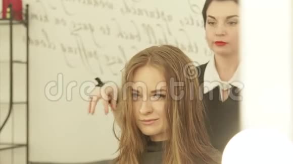 发型师在美发沙龙用吹风机干燥前梳理头发把剪发机的长发定型视频的预览图