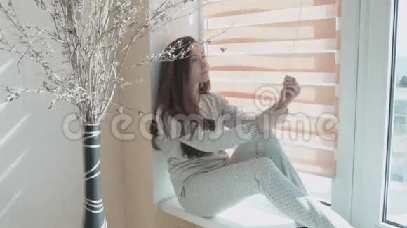 美丽的微笑的年轻女子是由滚筒百叶窗播放的那个女孩坐在窗台上视频的预览图