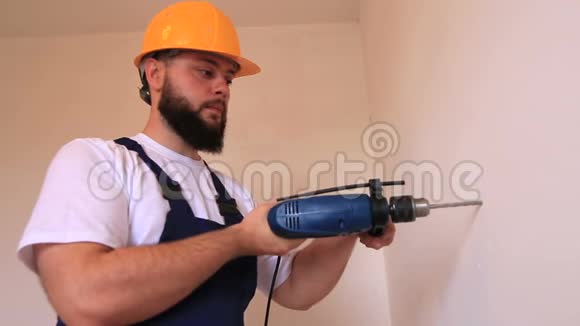 施工工人和杂工用蓝色电钻在施工现场的墙上钻一个钉子孔视频的预览图