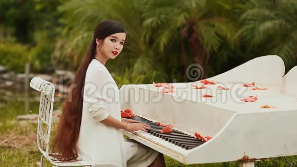 越南女孩留着长长的黑发在户外弹钢琴枫叶散落在钥匙上秋天的主题视频的预览图