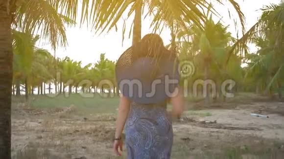 戴着蓝色帽子和眼镜的年轻女孩以热带椰子棕榈为背景中弹慢动作视频的预览图