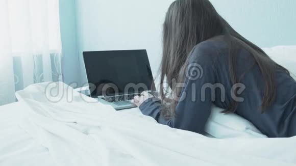 女商人带着笔记本在床上度假年轻女人用笔记本做生意白色床蓝色房间轻型视频的预览图