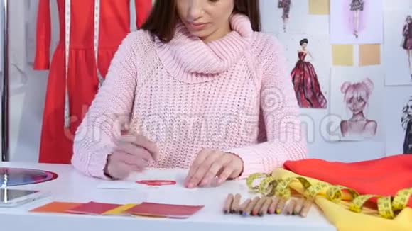 女设计师在桌子上画一件连衣裙的草图躺着织物样品关门视频的预览图