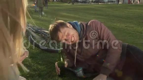 公园里一个微笑的年轻人躺在草坪上手里拿着一个瓶子快乐的人和朋友在公园里休息视频的预览图