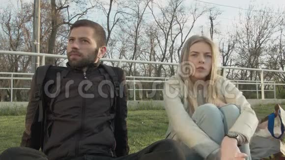 年轻漂亮的女人和坐在草坪上的年轻人说话年轻的一对学生讨论坐在视频的预览图