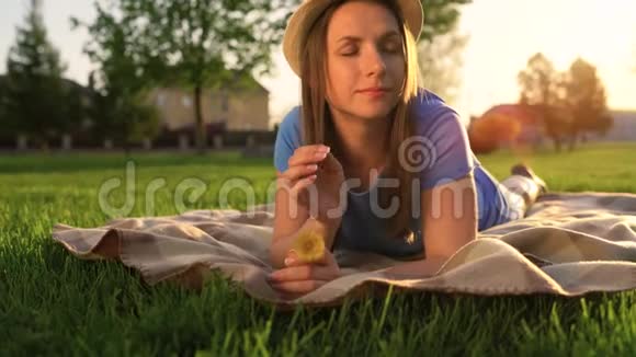 日落时分手里拿着蒲公英的女孩躺在公园的毯子上放松视频的预览图