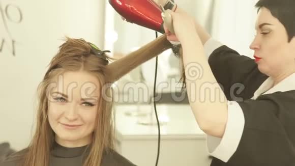 理发师在美容院用吹风机和刷子给女人做长发把剪发器烘干的女人视频的预览图