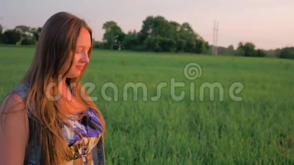 日落时分一位美丽的年轻女子站在绿色的田野上在大自然中微笑和放松带着呼吸视频的预览图
