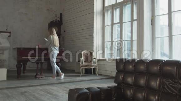 这位可爱的金发女郎拿着咖啡穿着白色袜子把手机拿在家里美丽的年轻女子视频的预览图