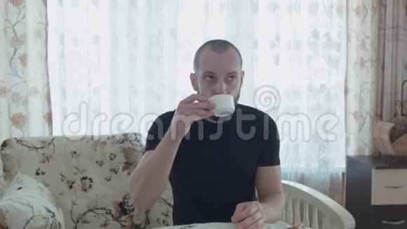 一个年轻英俊的男人正在早餐喝咖啡他站起来走到窗户打开窗户视频的预览图