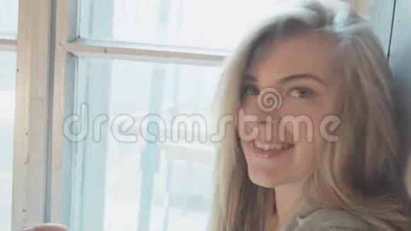 年轻快乐的女孩看着相机微笑微笑美丽的金发女郎坐在窗口写短信视频的预览图