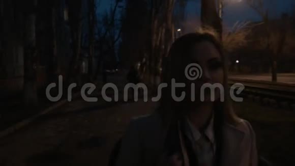一个漂亮的金发女郎晚上沿着一条黑暗的街道走着一个走路的年轻女人的特写视频的预览图