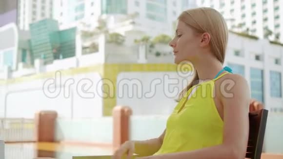 穿着黄色衣服的女人坐在游泳池附近的椅子上从塑料瓶喝水视频的预览图