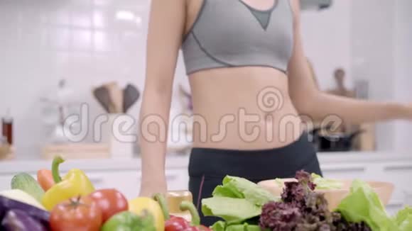 年轻的亚洲妇女做沙拉健康的食物同时使用平板电脑寻找食谱在厨房视频的预览图
