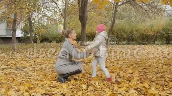 妈妈在一个秋天的公园里围着一个孩子转快乐的母女在秋天公园散步视频的预览图