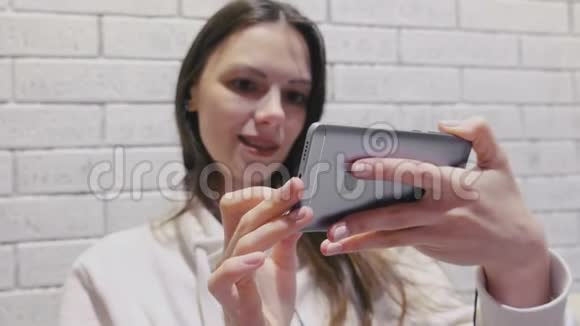 美丽的黑发女人看着一个系列耳机在手机上的砖墙背景视频的预览图