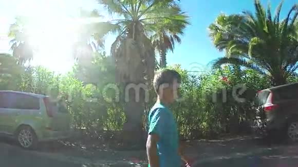 男孩带着棕榈树和夹竹桃沿着小巷走视频的预览图