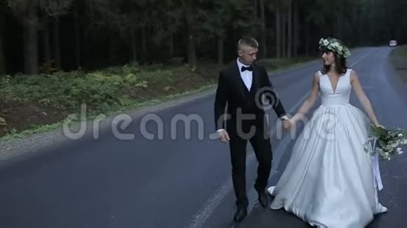 那人和他的新娘正牵着手沿着马路穿过高大的树视频的预览图