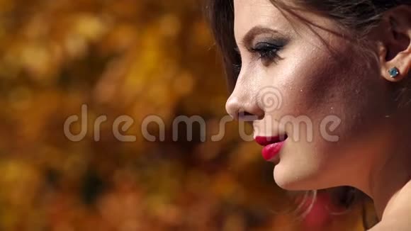 一个美丽的女孩的特写在秋天的公园里散步化妆鲜艳视频的预览图