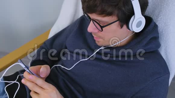 男人在智能手机上用耳机听音乐坐在扶手椅上唱一首歌视频的预览图
