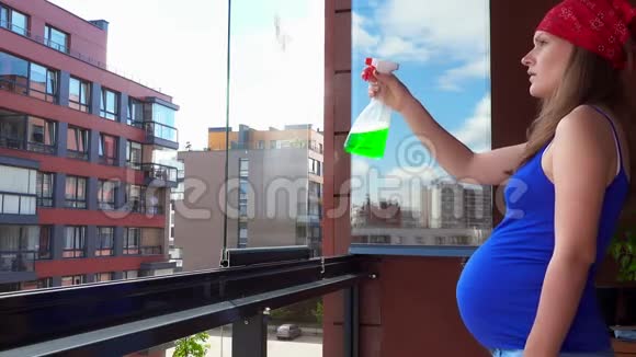 孕妇在家庭阳台用抹布和清洁剂擦拭窗户视频的预览图