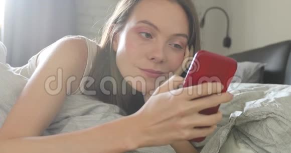 快乐的女人躺在床上微笑的文本智能手机视频的预览图