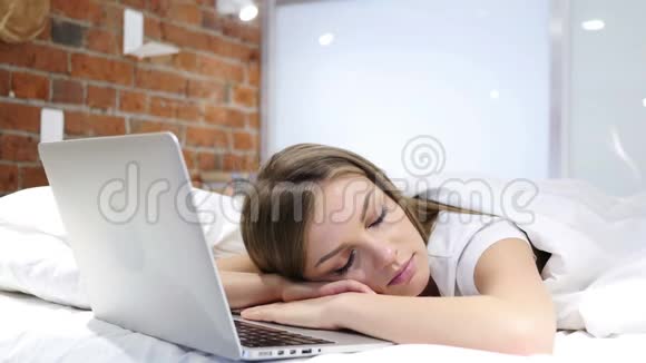 下班后睡在靠近笔记本电脑的床上的女人视频的预览图