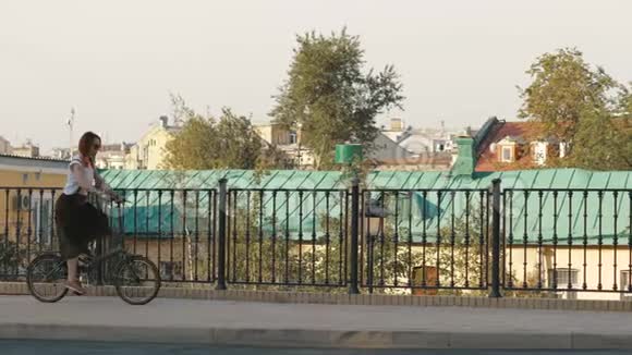 红发妇女骑自行车在城市的背景建筑和屋顶房子视频的预览图