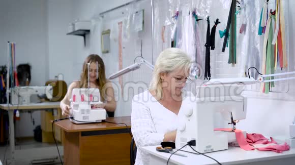 两名妇女从事服装制造穿着白色西装的女人坐在前台在现代服装上缝制粉红色的布视频的预览图