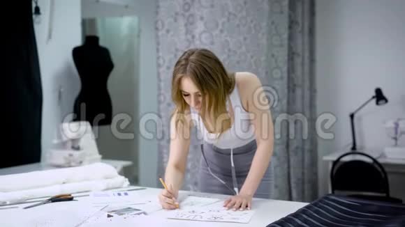 年轻女子站在桌子上在裁剪工作室和素描未来的服装设计新设计视频的预览图