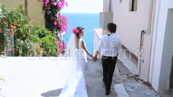 结婚纪念日新娘和新郎在一条鲜花盛开的美丽街道上出海视频的预览图