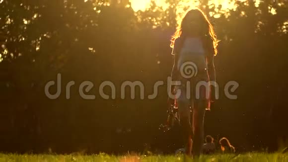 年轻女子赤脚走在草地上手里拿着高跟鞋4K变焦镜头夏日夕阳视频的预览图