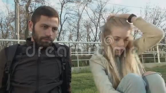 两个学生在草坪上的年轻人和年轻漂亮的女孩这对夫妇听着幕后的人点头视频的预览图
