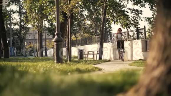 红色头发的年轻女子在公园底景骑自行车女子自行车公园视频的预览图