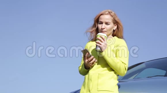自信的年轻商务女性在她的车附近喝咖啡正在打手机视频的预览图