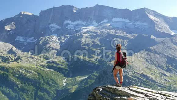 女子站在山顶高海拔岩石景观与冰川和高峰的背景夏日冒险视频的预览图