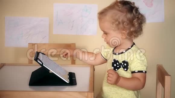 可爱的小女孩用平板电脑坐在桌子附近视频的预览图