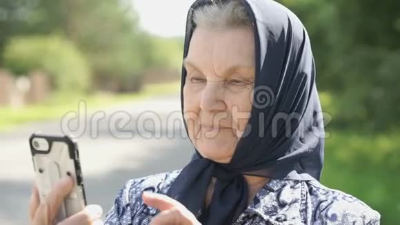 微笑成熟的老妇人在户外展示智能手机视频的预览图