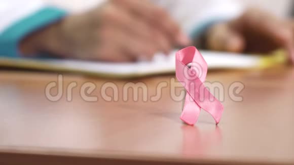 一位医生桌子上的粉红色丝带乳腺癌意识符号视频的预览图
