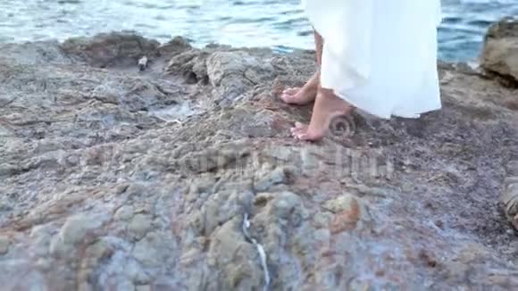 穿着白色衣服的漂亮女孩站在海边的石头上希腊视频的预览图
