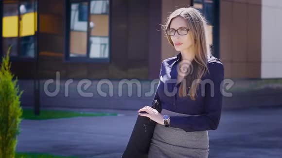 穿着蓝色衬衫和灰色裙子的年轻漂亮女士正在户外散步沿着现代办公楼和视频的预览图