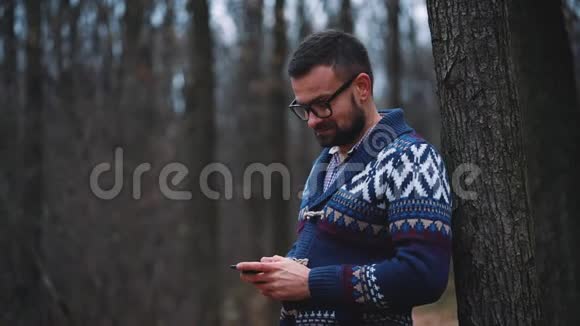 戴眼镜的人正穿过秋天的森林使用智能手机慢动作视频的预览图
