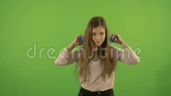 一个漂亮的年轻白人模特通过耳机和舞蹈听音乐在绿色的背景上视频的预览图