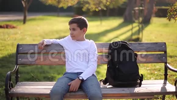 穿白色毛衣的少年坐在长凳上带背包的帅哥学校男孩视频的预览图