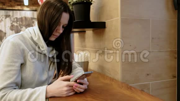 穿着一件亮衬衫的年轻黑发女人坐在咖啡馆里用手机上网视频的预览图