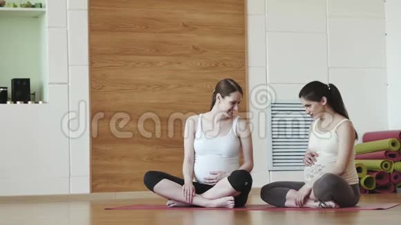 两个快乐的孕妇坐在垫子上在健身房里聊天视频的预览图
