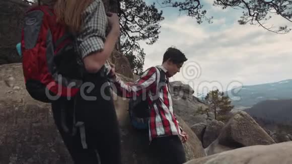 年轻人爬山牵着手在岩石的顶端有一个人指着什么女孩视频的预览图